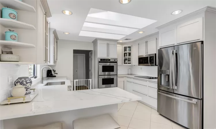 Kitchen featuring white cabinetry, sink, kitchen peninsula, stainless steel appliances, and light stone counters