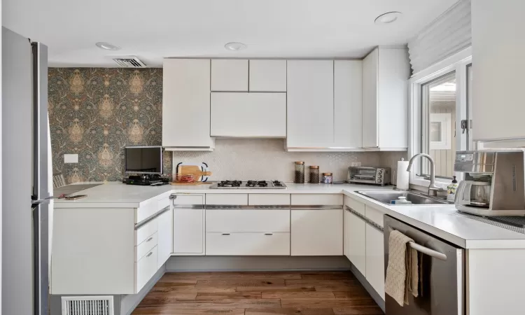 Kitchen with sink, backsplash, white cabinetry, and appliances with stainless steel finishes