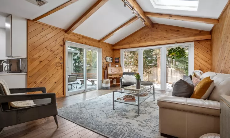 Living room with vaulted ceiling with skylight, light hardwood / wood-style flooring, and wooden walls