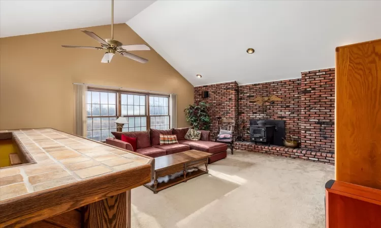 Carpeted living room featuring a wood stove, high vaulted ceiling, and ceiling fan