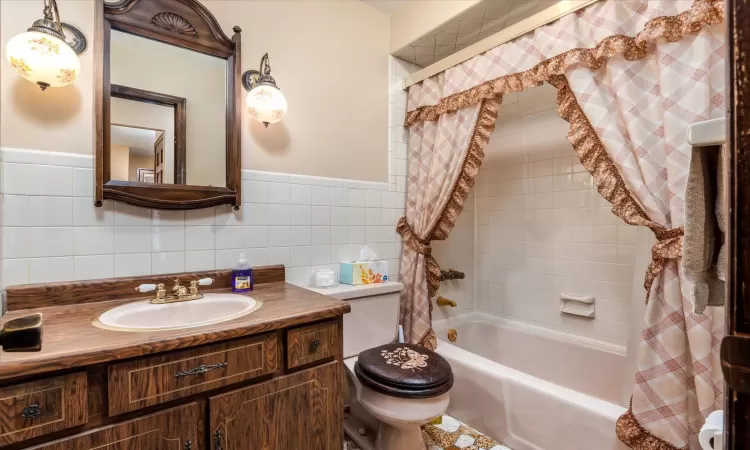 Full bathroom with vanity, toilet, tile walls, and shower / bathtub combination with curtain