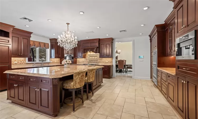 Kitchen with a large island with sink, premium range hood, an inviting chandelier, a breakfast bar area, and light stone counters