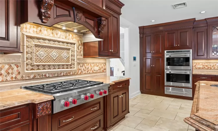 Kitchen with light stone countertops, backsplash, appliances with stainless steel finishes, and custom exhaust hood