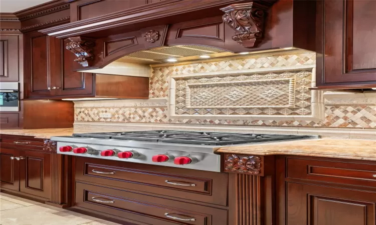 Kitchen featuring stainless steel gas stovetop, light tile patterned floors, custom exhaust hood, and light stone counters