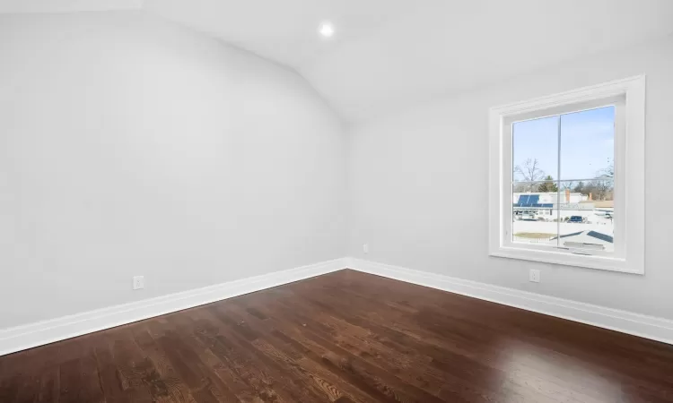 Spare room featuring hardwood / wood-style flooring and vaulted ceiling