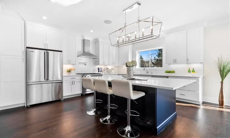 Kitchen featuring wall chimney range hood, white cabinets, and high quality appliances