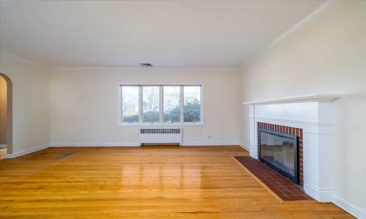 Unfurnished living room with light wood-type flooring, radiator heating unit, crown molding, and a fireplace