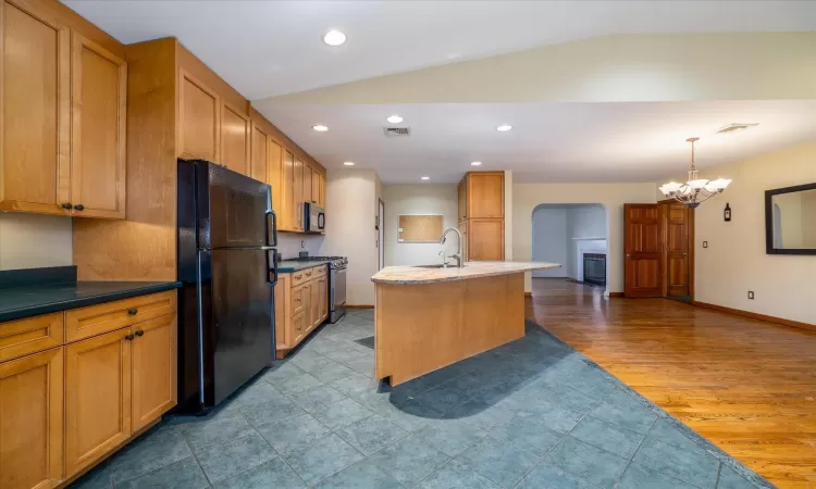 Kitchen with black appliances, pendant lighting, vaulted ceiling, and an island with sink