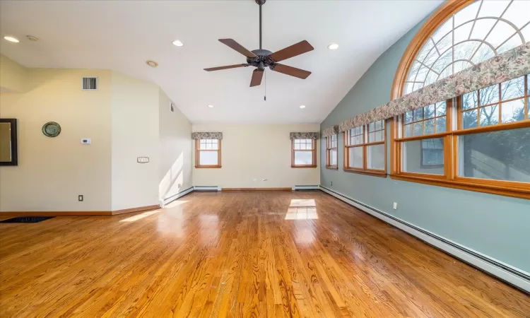 Unfurnished living room featuring ceiling fan, high vaulted ceiling, hardwood / wood-style floors, and a baseboard radiator