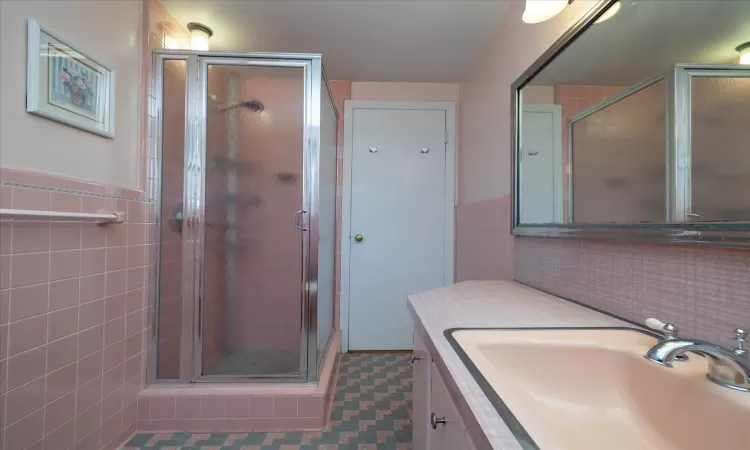 Bathroom with tile walls, a shower with shower door, and vanity