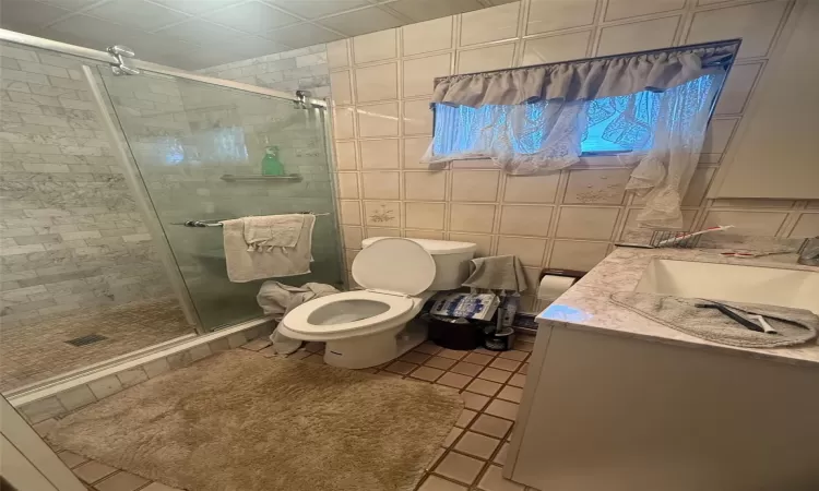 Bathroom with tile patterned floors, tile walls, toilet, walk in shower, and vanity