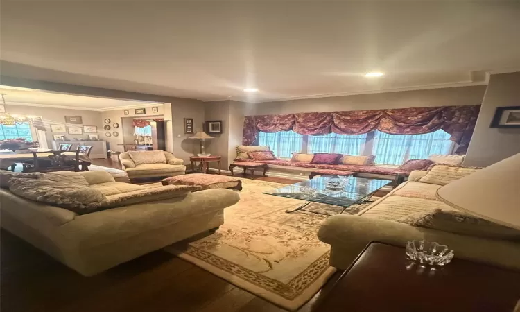 Living room featuring wood-type flooring, crown molding, and an inviting chandelier