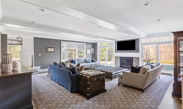 Living room featuring a wealth of natural light, a high end fireplace, ornamental molding, and beamed ceiling