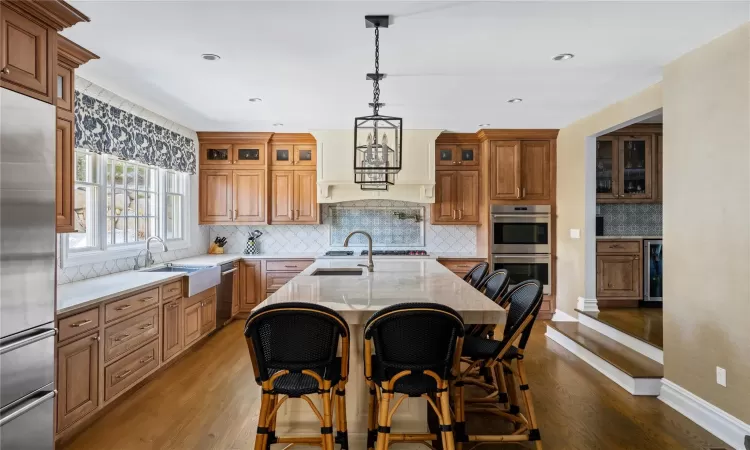 Kitchen with appliances with stainless steel finishes, sink, hanging light fixtures, hardwood / wood-style flooring, and a center island with sink