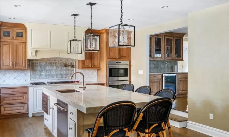 Kitchen with light stone countertops, a kitchen island with sink, sink, dark hardwood / wood-style floors, and beverage cooler