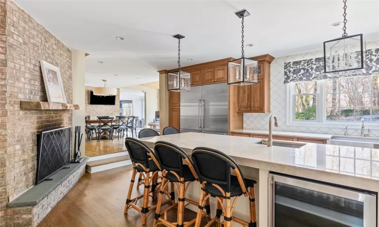 Kitchen with wine cooler, a fireplace, stainless steel built in refrigerator, a kitchen breakfast bar, and light stone counters