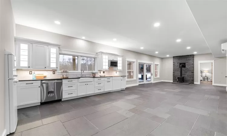 Kitchen with dishwasher, decorative backsplash, white cabinetry, a wood stove, and white refrigerator