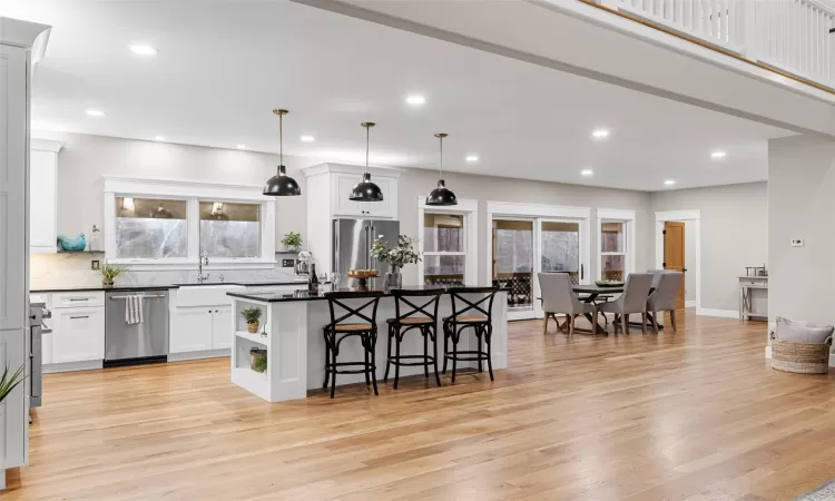 Kitchen featuring decorative light fixtures, light hardwood / wood-style floors, a kitchen island, stainless steel appliances, and white cabinets