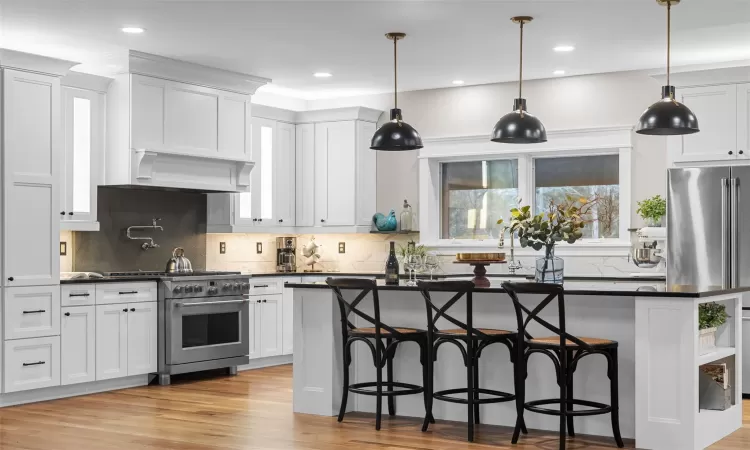 Kitchen with high end stainless steel range, premium range hood, white cabinetry, and a center island