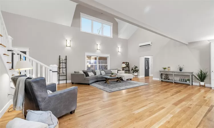 Living room featuring high vaulted ceiling, light wood-type flooring, and a wall mounted air conditioner