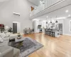 Living room with light hardwood / wood-style floors, a towering ceiling, and an AC wall unit