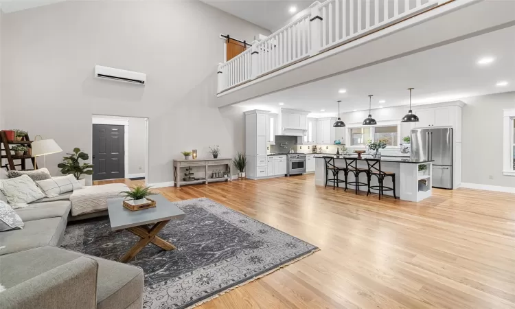 Living room with light hardwood / wood-style floors, a towering ceiling, and an AC wall unit