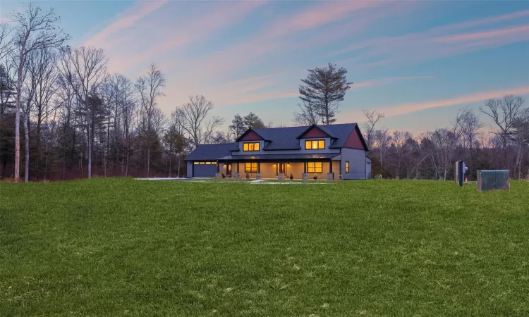 Back house at dusk featuring a garage and a lawn