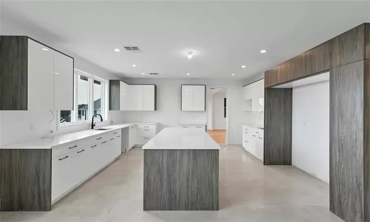 Kitchen with a center island, white cabinetry, sink, and light tile flooring