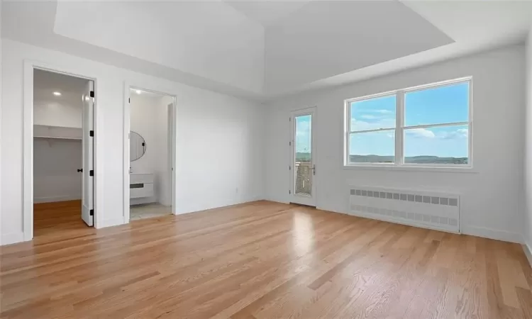 Master bedroom bedroom with a walk in closet, ensuite bathroom, radiator heating unit, and light hardwood / wood-style flooring