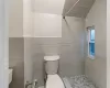 Bathroom with a tile shower, vaulted ceiling, toilet, and tile walls