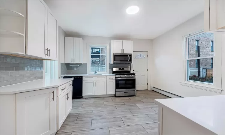 Kitchen with decorative backsplash, stainless steel appliances, baseboard heating, sink, and white cabinets