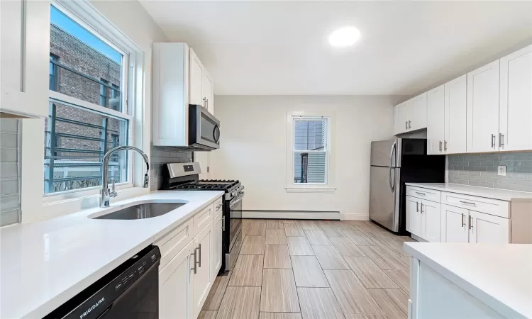 Kitchen featuring appliances with stainless steel finishes, backsplash, baseboard heating, sink, and white cabinets