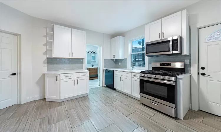 Kitchen featuring decorative backsplash, white cabinetry, sink, and stainless steel appliances