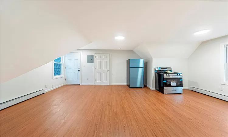 Unfurnished Living Room featuring light wood-type flooring, vaulted ceiling, and a baseboard heating unit