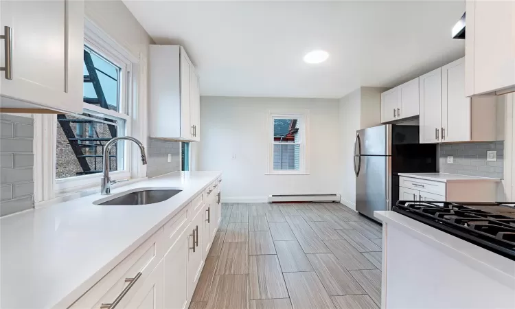 Kitchen featuring stainless steel fridge, backsplash, baseboard heating, sink, and white cabinetry