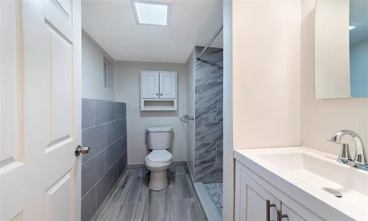 Basement Bathroom featuring tiled shower, vanity, tile walls, and toilet