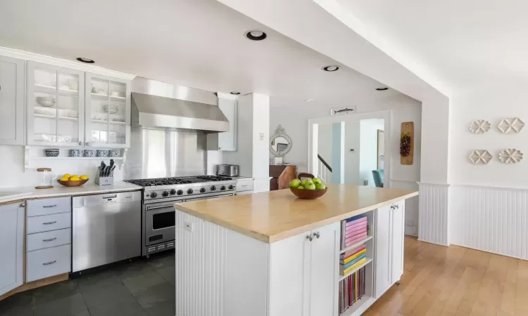 Kitchen featuring a center island, butcher block counters, appliances with stainless steel finishes, white cabinetry, and wall chimney exhaust hood