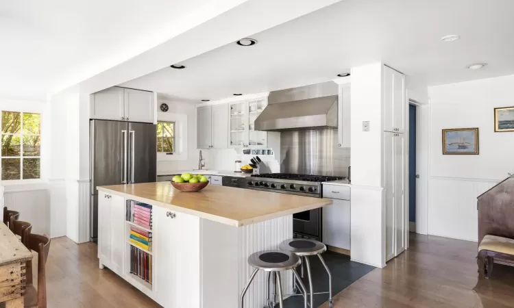 Kitchen featuring premium appliances, a center island, wall chimney range hood, a healthy amount of sunlight, and a kitchen breakfast bar