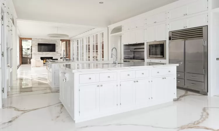 Kitchen with sink, white cabinets, stainless steel built in refrigerator, and an island with sink