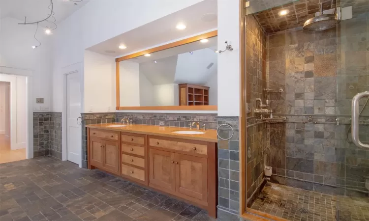 Bathroom featuring double vanity, tasteful backsplash, tile walls, vaulted ceiling, and a shower with shower door