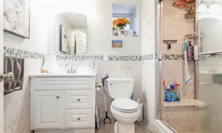 Bathroom featuring tile walls, an enclosed shower, vanity, and toilet