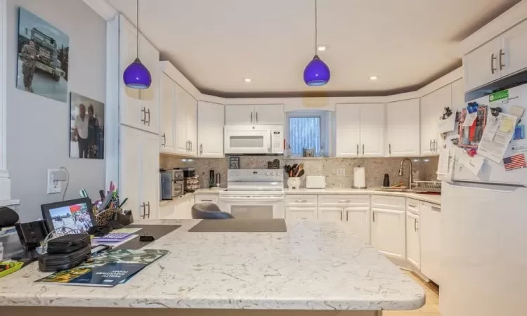 Kitchen featuring sink, white appliances, decorative light fixtures, and white cabinets