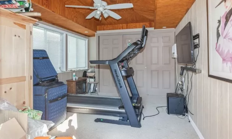 Workout area with wood walls, wood ceiling, light carpet, a raised ceiling, and ceiling fan