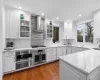 Kitchen with white cabinets, backsplash, light stone counters, stainless steel appliances, and wall chimney range hood