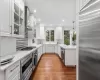 Kitchen with dark wood-type flooring, white cabinetry, built in appliances, decorative light fixtures, and light stone countertops