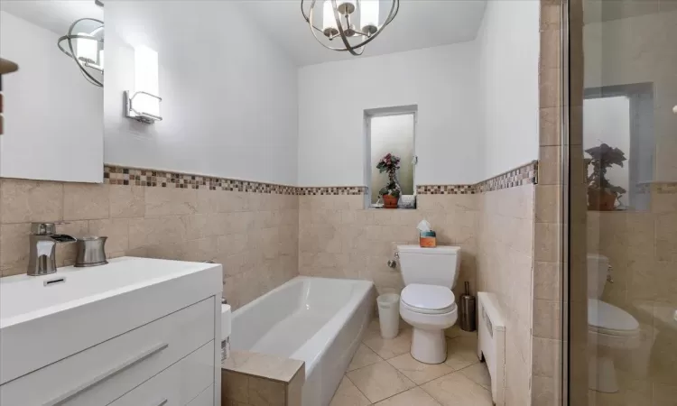 Bathroom with radiator, tile walls, tile patterned flooring, toilet, and a bath