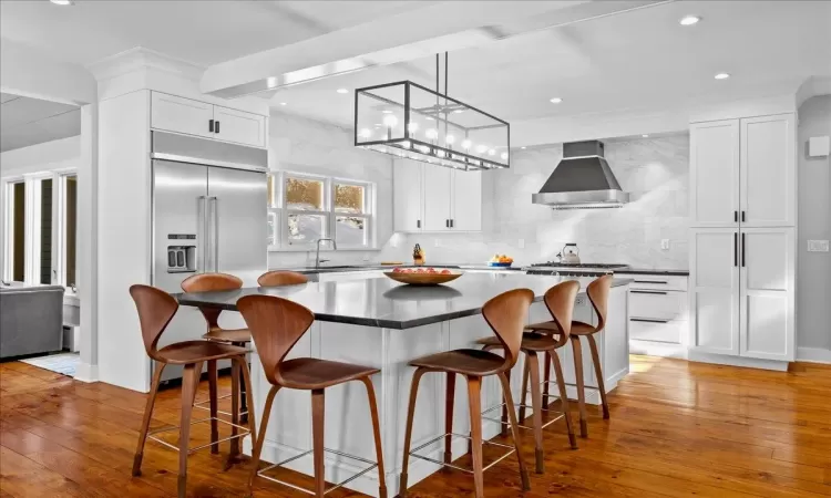 Kitchen featuring decorative backsplash, white cabinetry, range with gas cooktop, and wall chimney exhaust hood