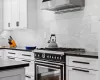 Kitchen featuring white cabinets, wall chimney exhaust hood, stainless steel built in refrigerator, tasteful backsplash, and light wood-type flooring