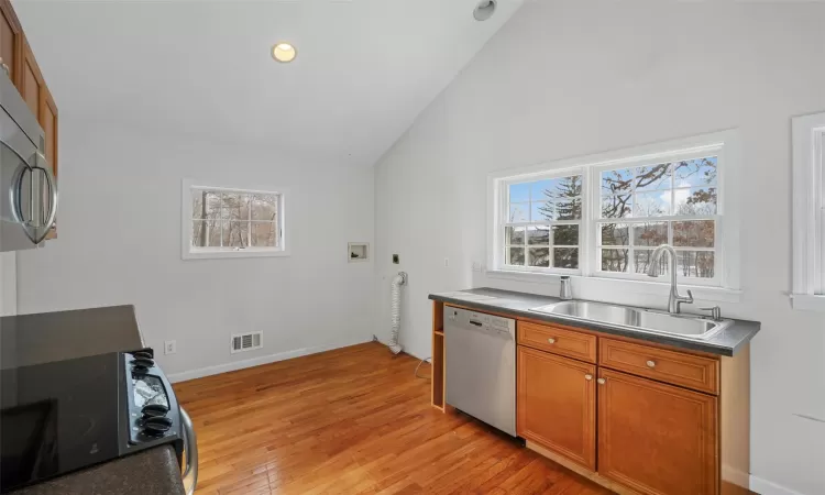 Kitchen featuring sink, appliances with stainless steel finishes, lofted ceiling, and light wood-type flooring