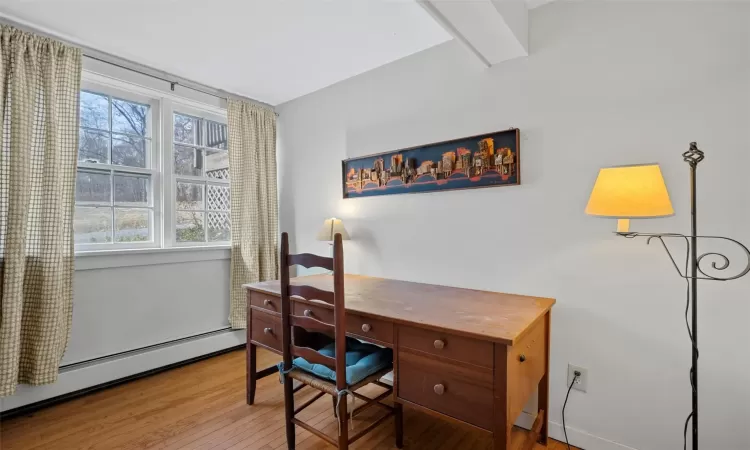 Office in lower level with beam ceiling, baseboard heating, and light hardwood / wood-style flooring